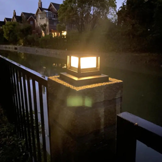 Decorative outdoor light fixture on a stone pedestal with a house in the background.