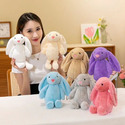 Woman holding a white plush bunny with colorful plush bunnies on a table.